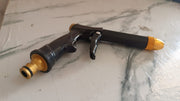 Brass water spray gun attached to a hose, powerfully spraying water during outdoor cleaning.