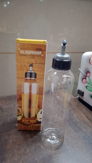 Hand holding the clear 1L oil dispenser, demonstrating its easy-pour function.