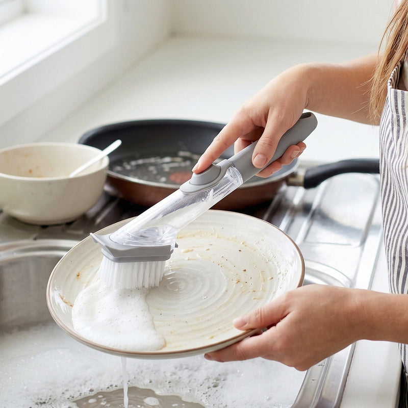 Hand holding soap dispensing dish scrub brush during cleaning