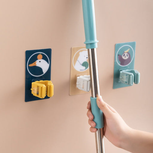 A white self-adhesive mop holder securely gripping a broom handle on a tiled wall.
