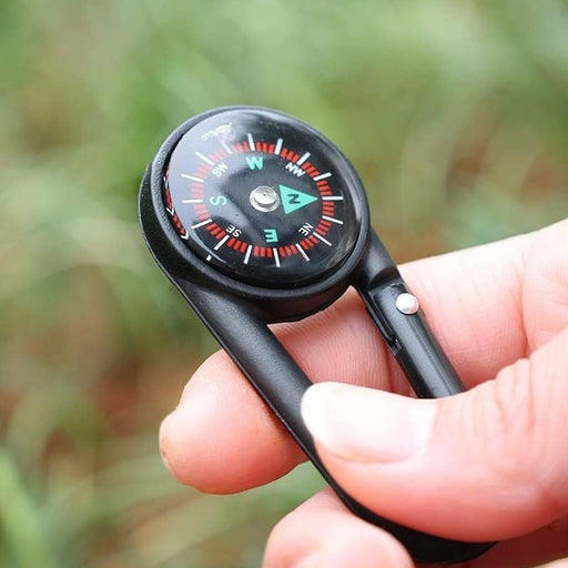 Mini compass with clip attached to a backpack strap, showing its compact size for outdoor use.